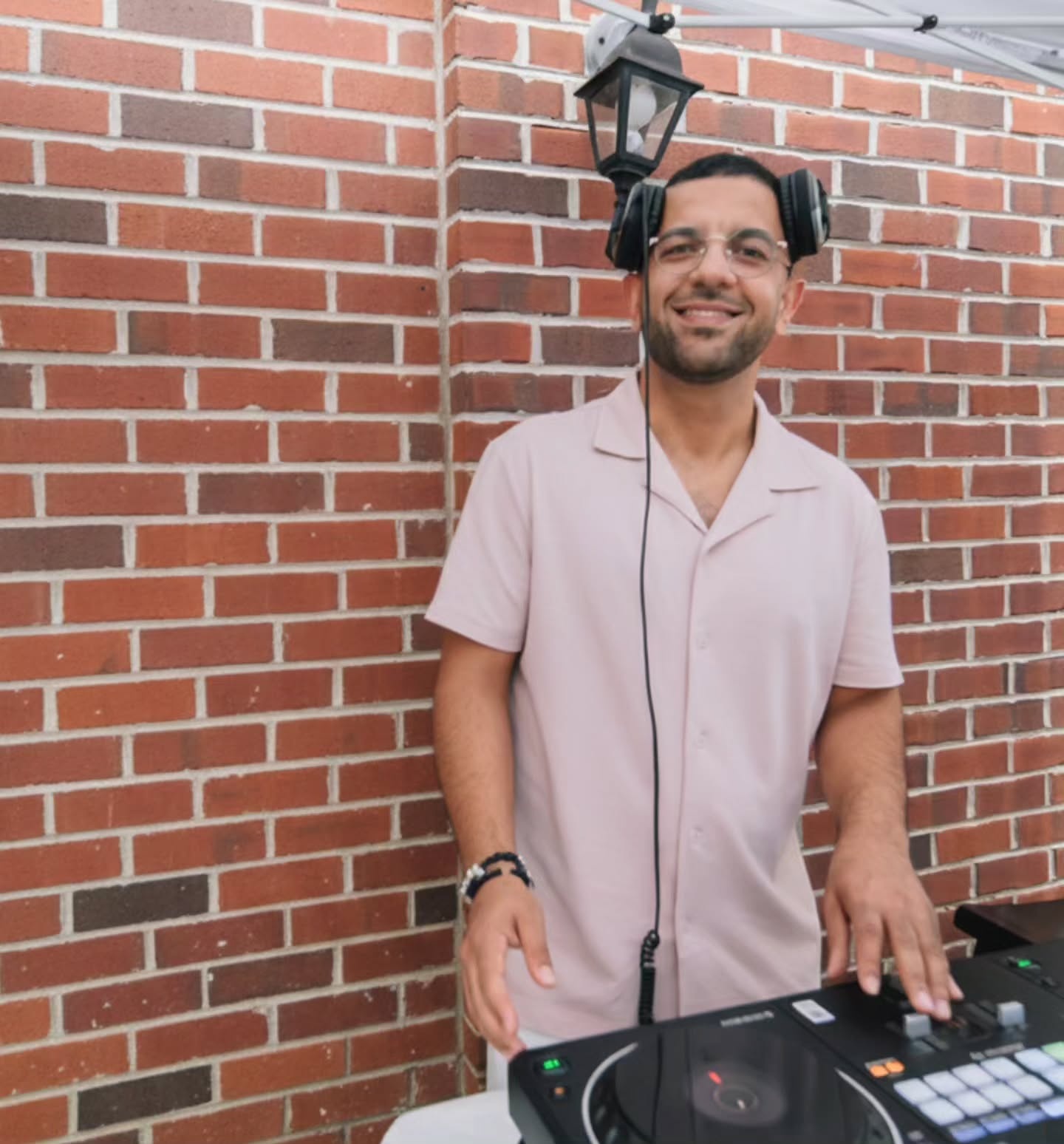 Armin Faraji smiling behind his DJ controller in front of a red brick wall